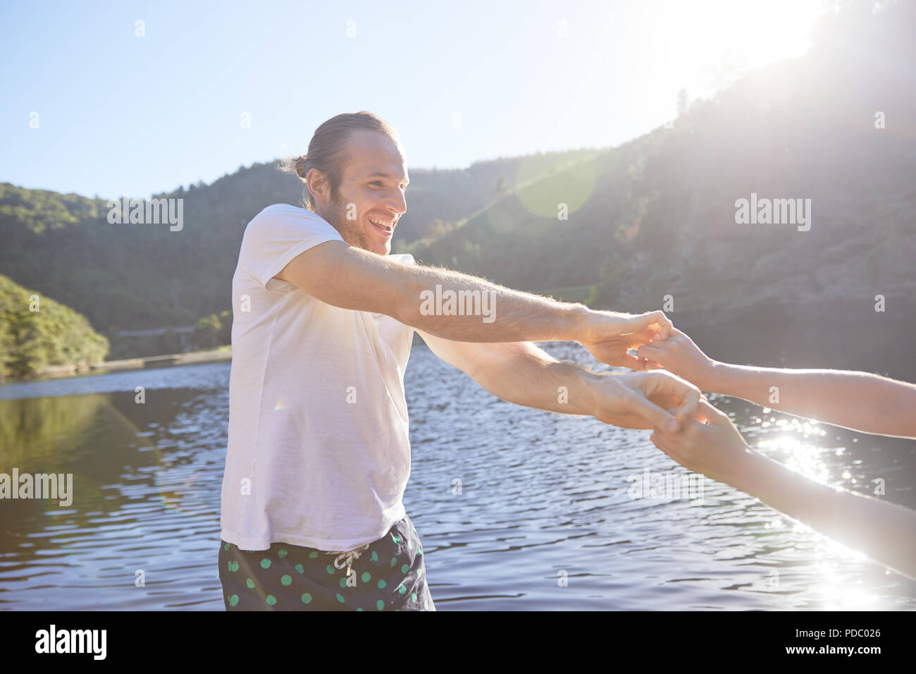Verspieltes Paar Hände halten am sonnigen Sommer See Stockfoto