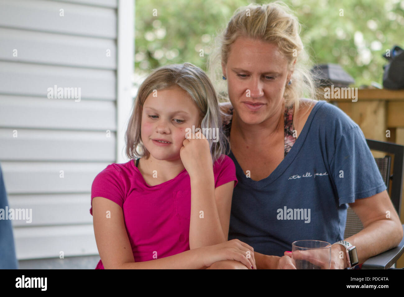 Attraktive, blonde Mutter und Tochter sitzen auf der Terrasse, in eine nachdenkliche Stimmung, sowohl auf der Suche nach unten, tief in Gedanken versunken. Beide Modell freigegeben Stockfoto