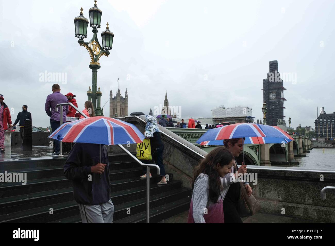 London, 9. August 2018: Touristen auf die Westminster Bridge Schutz vor dem Regen unter Regenschirmen. Credit: Claire Doherty/Alamy leben Nachrichten Stockfoto