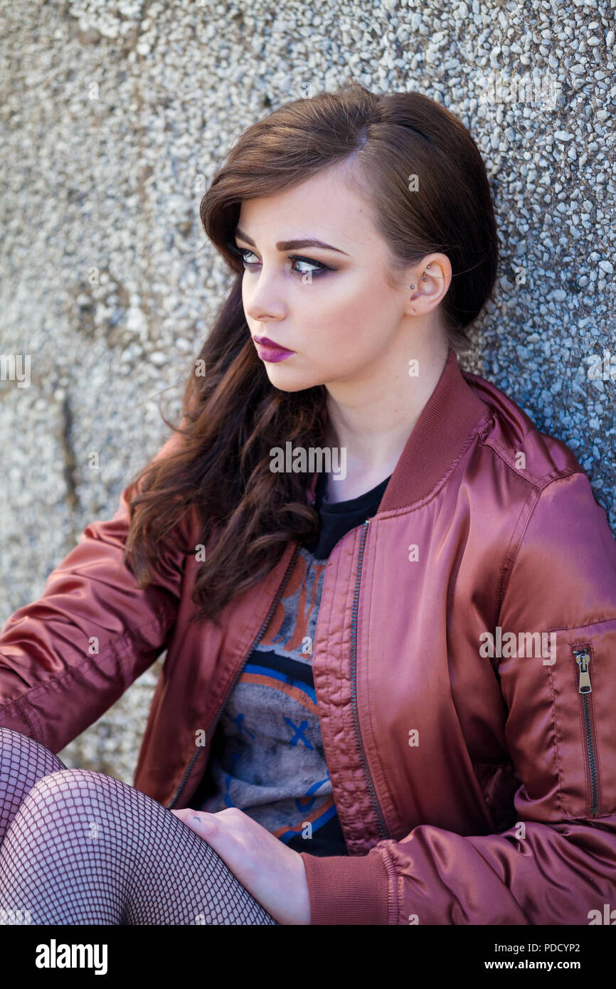 Eine alternative suchen Mädchen sitzen gegen eine Wand trägt eine glänzende  Bomberjacke Stockfotografie - Alamy