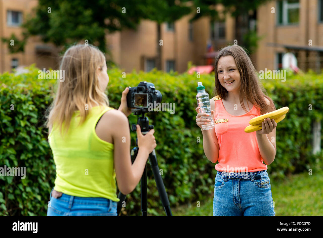 Mädchen Freundinnen in den Sommer im Park records Video auf der Kamera in einer gesunden Ernährung. Hände halten eine Banane Flasche Wasser fröhlich und glücklich lächelnd. Stockfoto