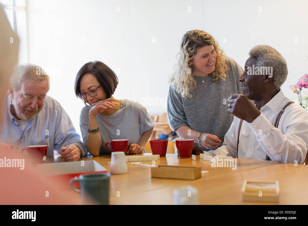 Ehrenamtliche im Gespräch mit älteren Menschen spielen am Tisch in der Mitte Stockfoto