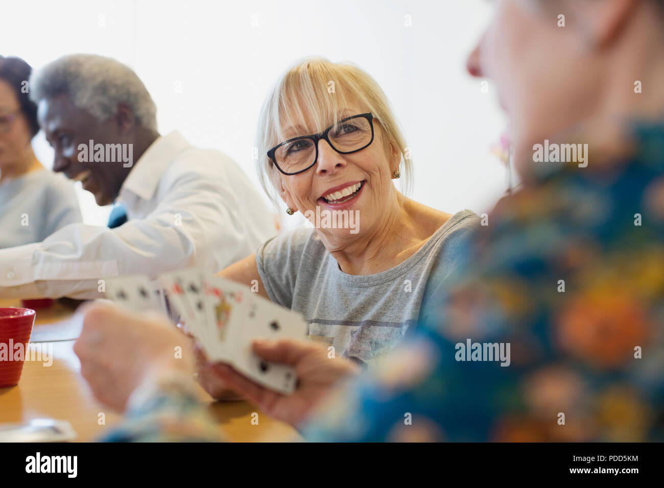 Lächelnd senior Frau Spielkarten mit Freund im Community Center Stockfoto