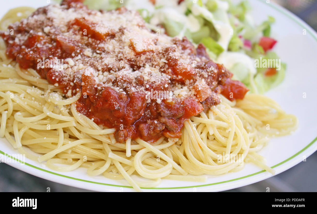 Gekochte spaghetti Pasta gekrönt mit einem köstlichen hausgemachten Soße und frisch geriebenem Parmesan und einem frischen Garten Salat garniert mit cremig Stockfoto