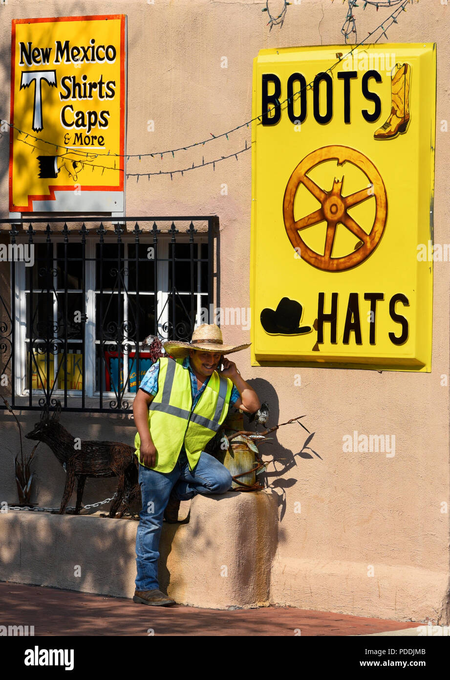 Ein ungelernter Arbeiter Gespräche über sein Smartphone neben einem Store verkaufen Western Boots und Cowboy Hüte in Santa Fe, New Mexico. Stockfoto