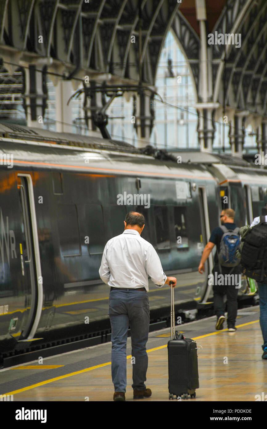 Person WHEELING ein Koffer entlang einer Plattform auf London Paddington Station seinen Zug zu bekommen Stockfoto