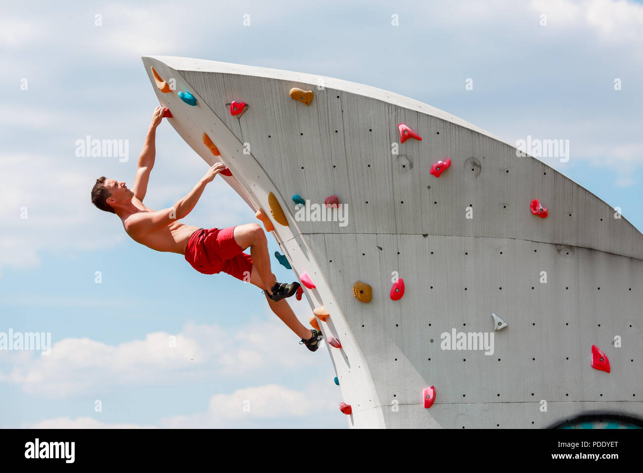 Foto der jungen Sportler in roten Hosen hängen an der Wand zum Klettern gegen den blauen Himmel mit Wolken Stockfoto