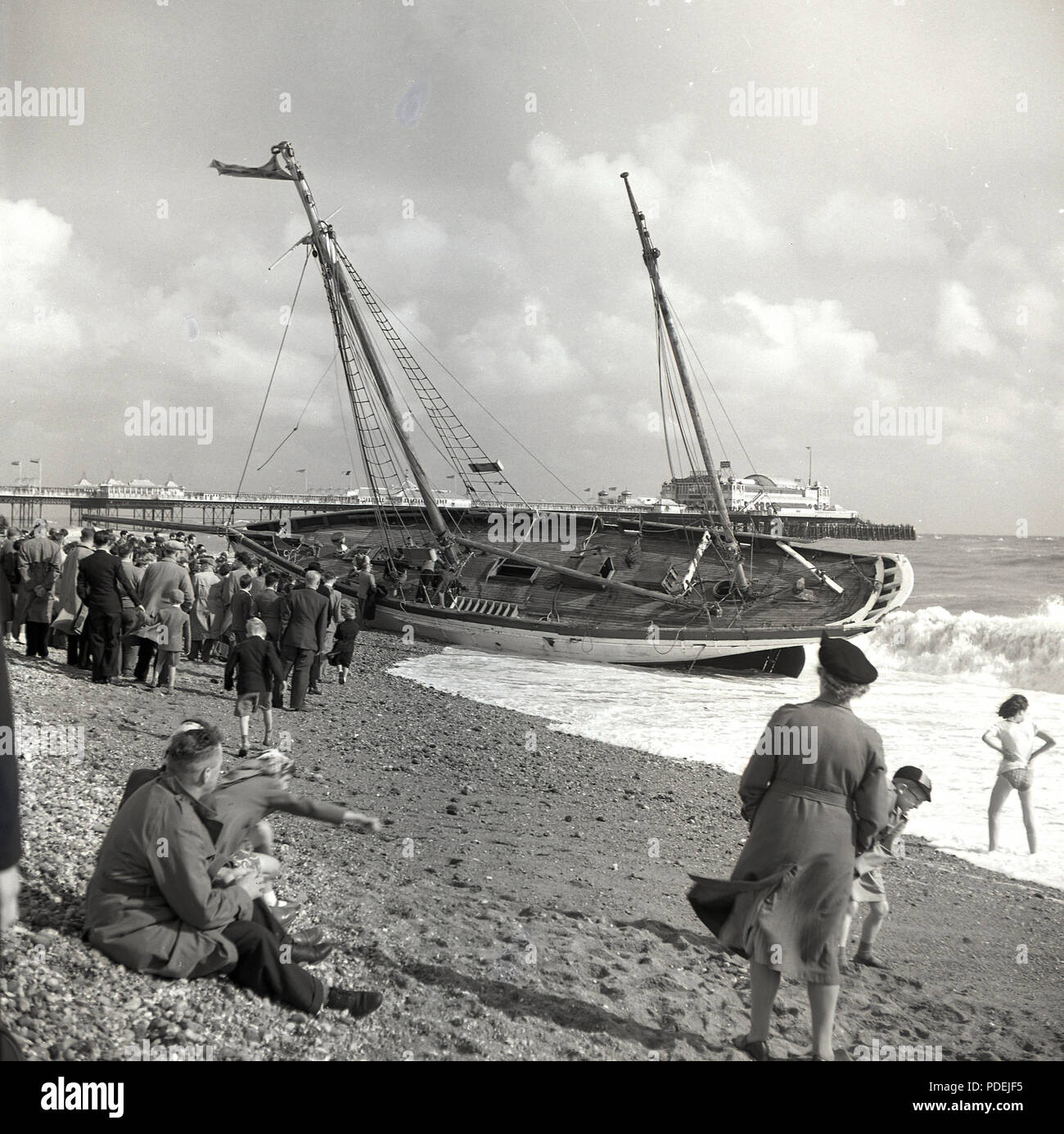 1950, historische, eine Menschenmenge versammelt, um zu sehen, ein großes Segelboot Angeschwemmten an Land am Meer in Brighton, England, UK. Stockfoto
