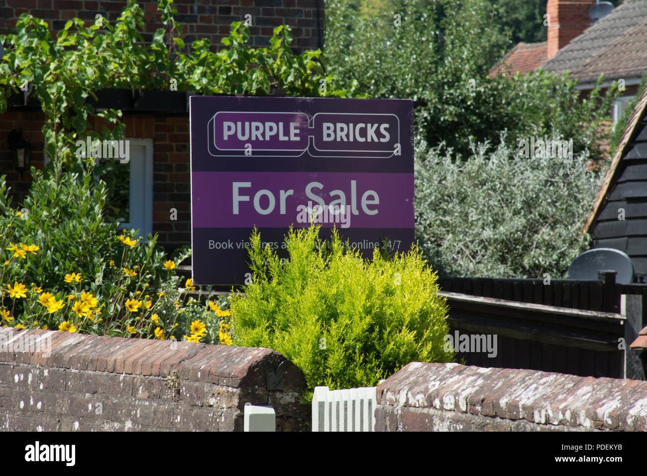 Lila Ziegel der Immobilienmakler für Verkauf Zeichen außerhalb eines Hauses in Surrey, Großbritannien Stockfoto