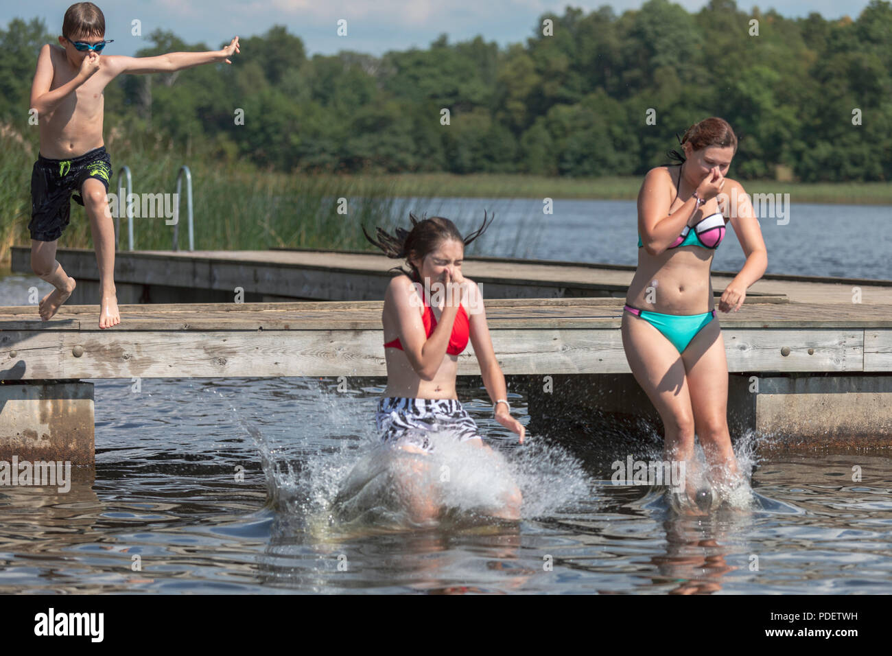 Auch, Schweden - 28. Juli 2018: Die Gruppe von Kindern, Jungen und zwei Mädchen im Teenageralter in See Wasser springen von Holzsteg Stockfoto