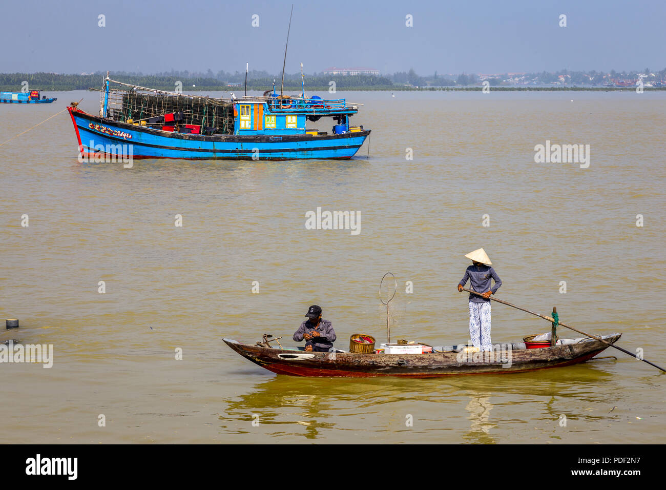 Mädchen mit langen oar Ihr kleines Boot bewegen vor einem trowler in einem Hoi ein Fischerdorf. Stockfoto