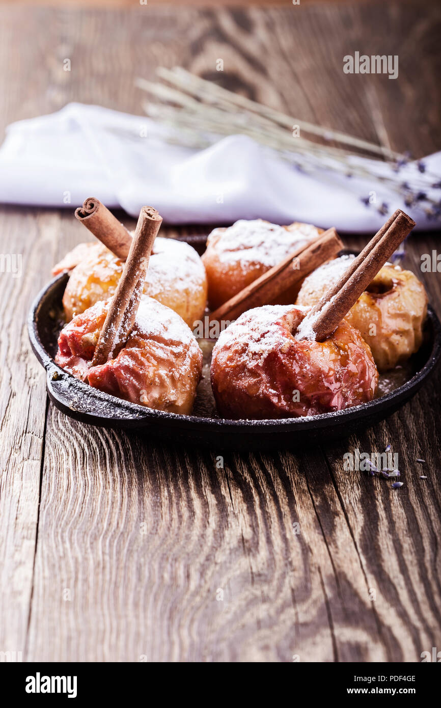 Gebackene Äpfel mit Zimtstangen in Gusseisen Skillet auf rustikalen Holztisch Stockfoto