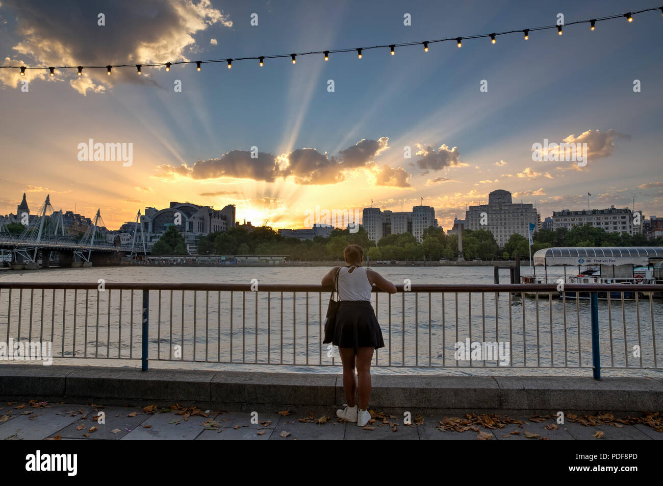 LONDON, Großbritannien - 6 August, 2018: Eine junge Frau am Südufer der Themse betrachtet die Sonnenstrahlen, während die Sonne hinter Charing Cross setzt Stockfoto