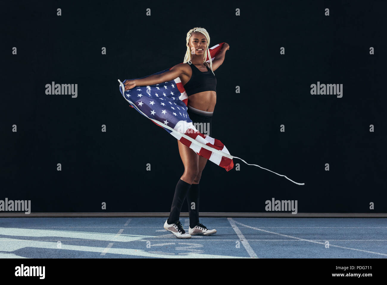 Weibliche Athleten gehen auf Laufbahn feiern Sieg Holding amerikanische Flagge. Sprinter zu Fuß auf der Laufstrecke, die die US-Flagge hinter ihr. Stockfoto