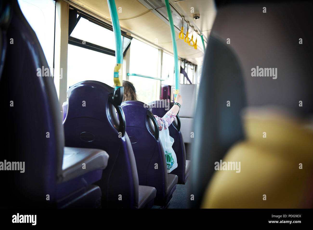Junge weiße Frau sitzt auf einem leeren Bus während der Fahrt zur Arbeit, mit einem Blick von den Rücksitzen Stockfoto