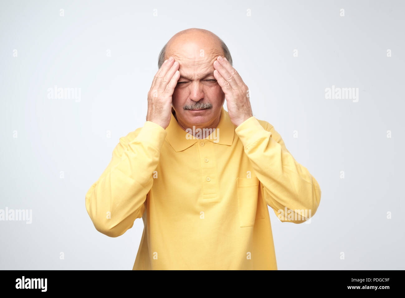 Nahaufnahme von reifer Mann im gelben T-Shirt mit geschlossenen Augen den Kopf berühren in den Schmerz. Gesundheitliche Probleme im Alter, Neuralgie Konzept Stockfoto