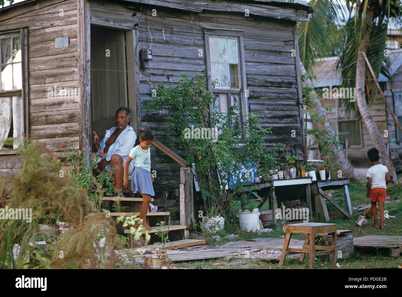 Belizean Mann in Türdurchgang mit Holz verkleidete Haus saß mit Kindern spielen im Freien, Belize City, Belize, Mittelamerika, Karibik Stockfoto