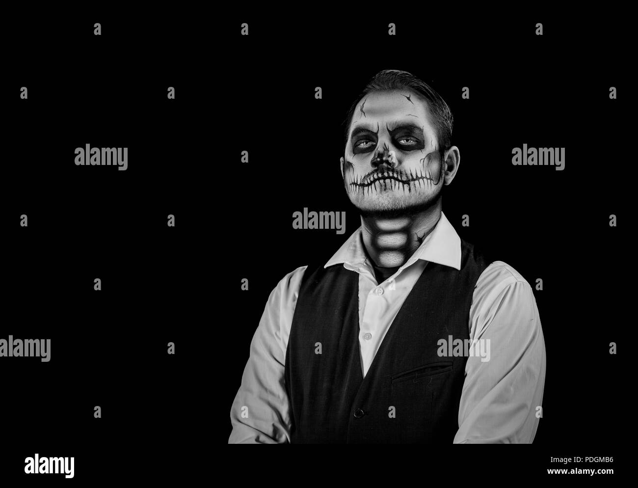 Porträt von einem gut gekleideten Mann mit Totenkopf Make-up. Horror und Halloween Motto, mit Bühnenbeleuchtung und Effekte. Bild in Schwarz und Weiß Stockfoto