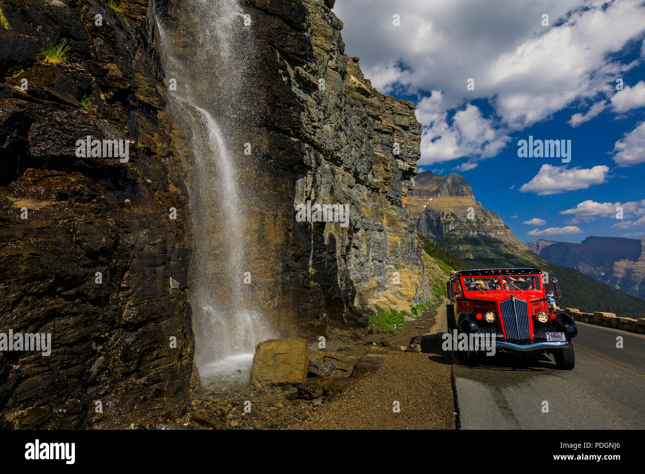 Eine tour bus ein Jammer stoppt mit einer Wagenladung von Menschen vor einem Wasserfall entlang der auf der Sonne Straße im Glacier National Park, Montana. Stockfoto