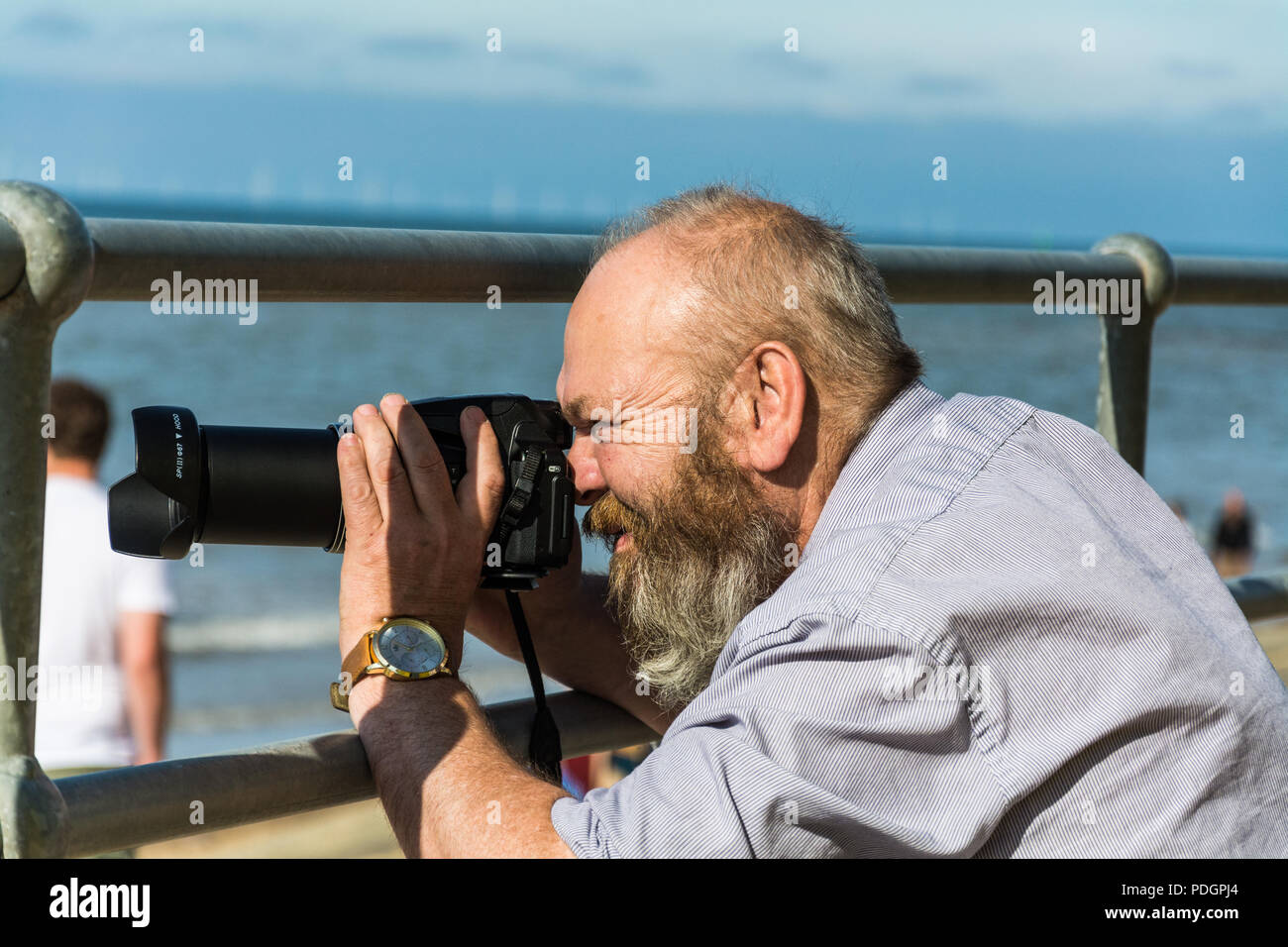 Ein bärtiger Mann die Bilder mit einer Nikon P900, Coolpix an einem sonnigen Tag am Strand, Prestatyn, Wales, UK. Stockfoto