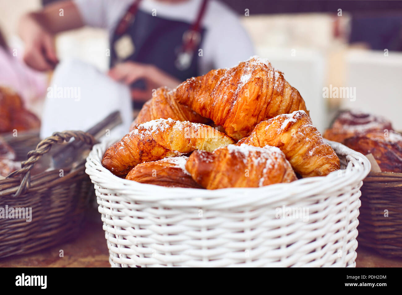 Junger Mann barista unter Croissant mit Zangen in Coffee Shop. Fokus auf Croissants Stockfoto