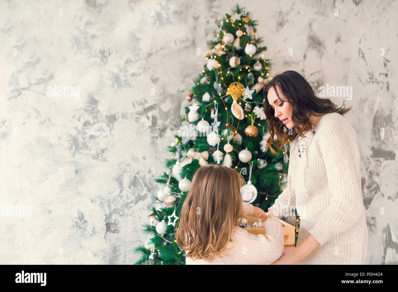 Frau mit ihrer Tochter, die eine Box mit viel Weihnachten silber Dekorationen in der Nähe der Weihnachtsbaum. Weihnachten Konzept Stockfoto