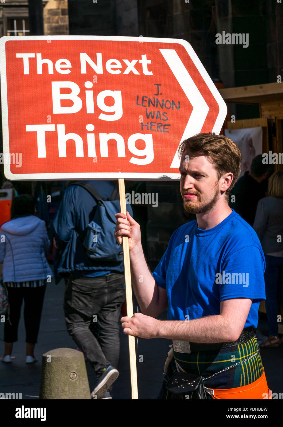 Edinburgh, Schottland, Großbritannien. 9. August 2018. Edinburgh Fringe Festival, Royal Mile, Edinburgh, Schottland, Vereinigtes Königreich. An einem sonnigen Festival Tag der Jungfrau Geld gesponsert Street Festival mit Menschen und fringe Darsteller verpackt ist. Ein Mann mit einem Pfeil Schild, das nächste große Ding Stockfoto