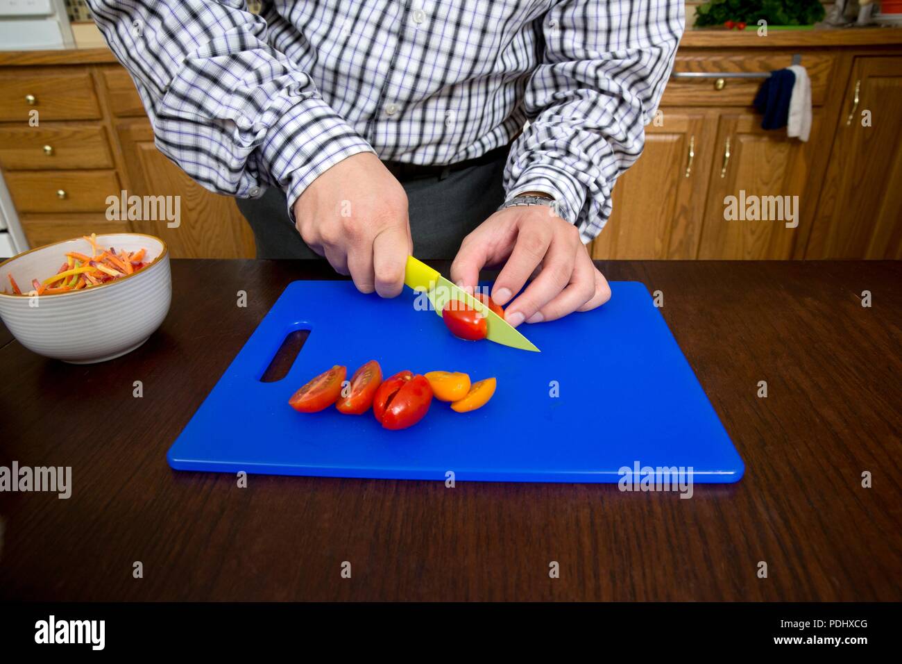 Man schneiden Tomaten mit einem schön auf einem blauen Schneidbrett in einer Küche zu Hause Stockfoto