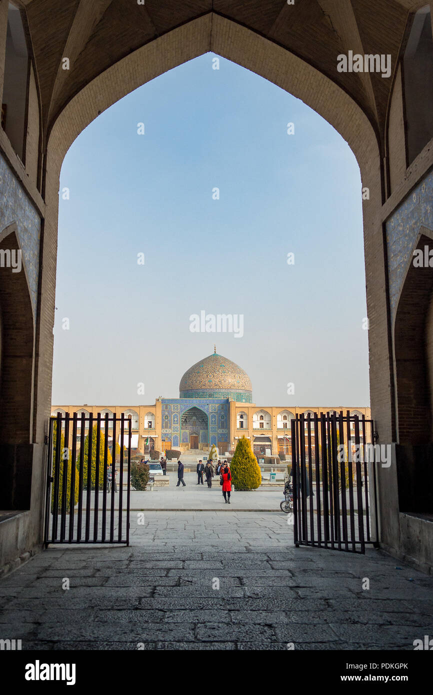 Eine Frau in einem roten Mantel hält für ein Foto vor der beeindruckenden und bunte Kuppel der Sheikh Lotfollah Moschee in Naqsh-e-Jahan Square, Isfahan, Stockfoto