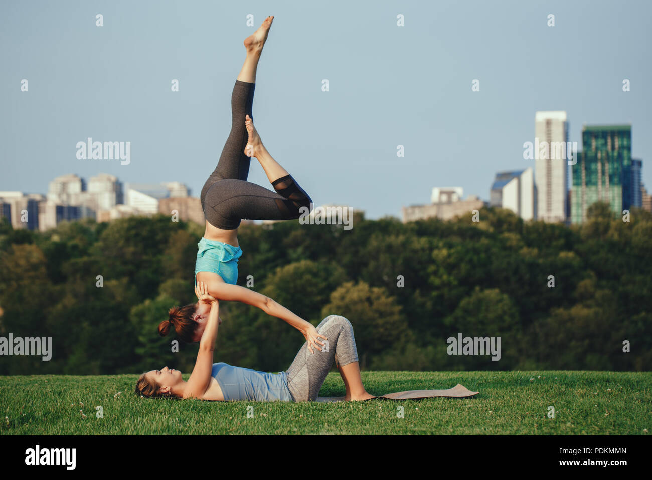 Zwei kaukasischen Frauen Yogi tun Schulter Leuchter acro Yoga dar. Frauen tun stretching Training im Park im Freien bei Sonnenuntergang. Gesunder Lebensstil Stockfoto