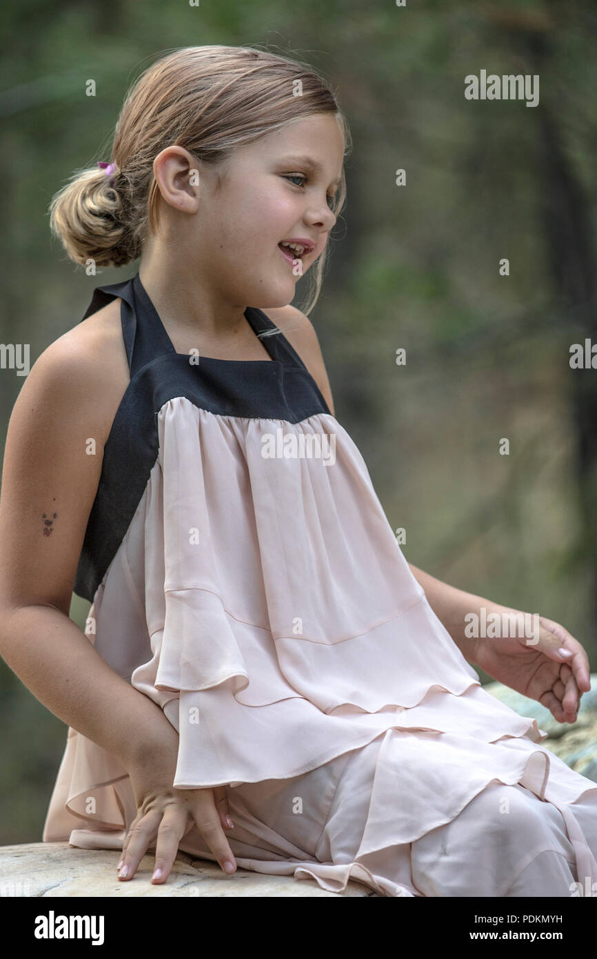 Attraktive junge Mädchen, in der High fashion dress, posierend auf großen Felsen mit Rose in der Hand. Lächelnd an Kamera mit ein paar Zähne fehlen. Vertikale und Mo Stockfoto