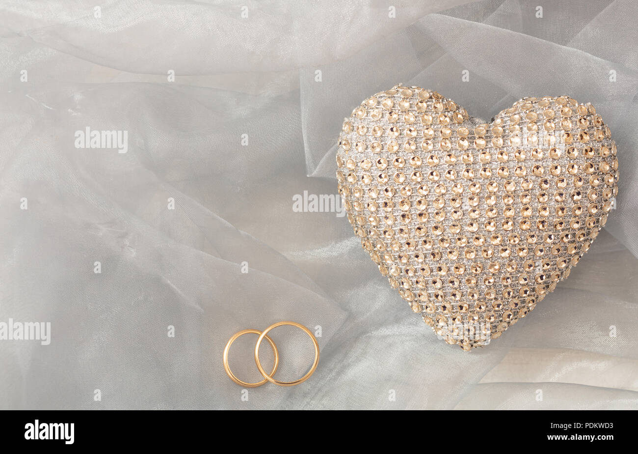 Liebe und Ehe Konzept. Goldene Hochzeit Ringe und Pailletten Herz, Ansicht von oben, kopieren, auf einem weißen seidigen Tüll Hintergrund. Stockfoto