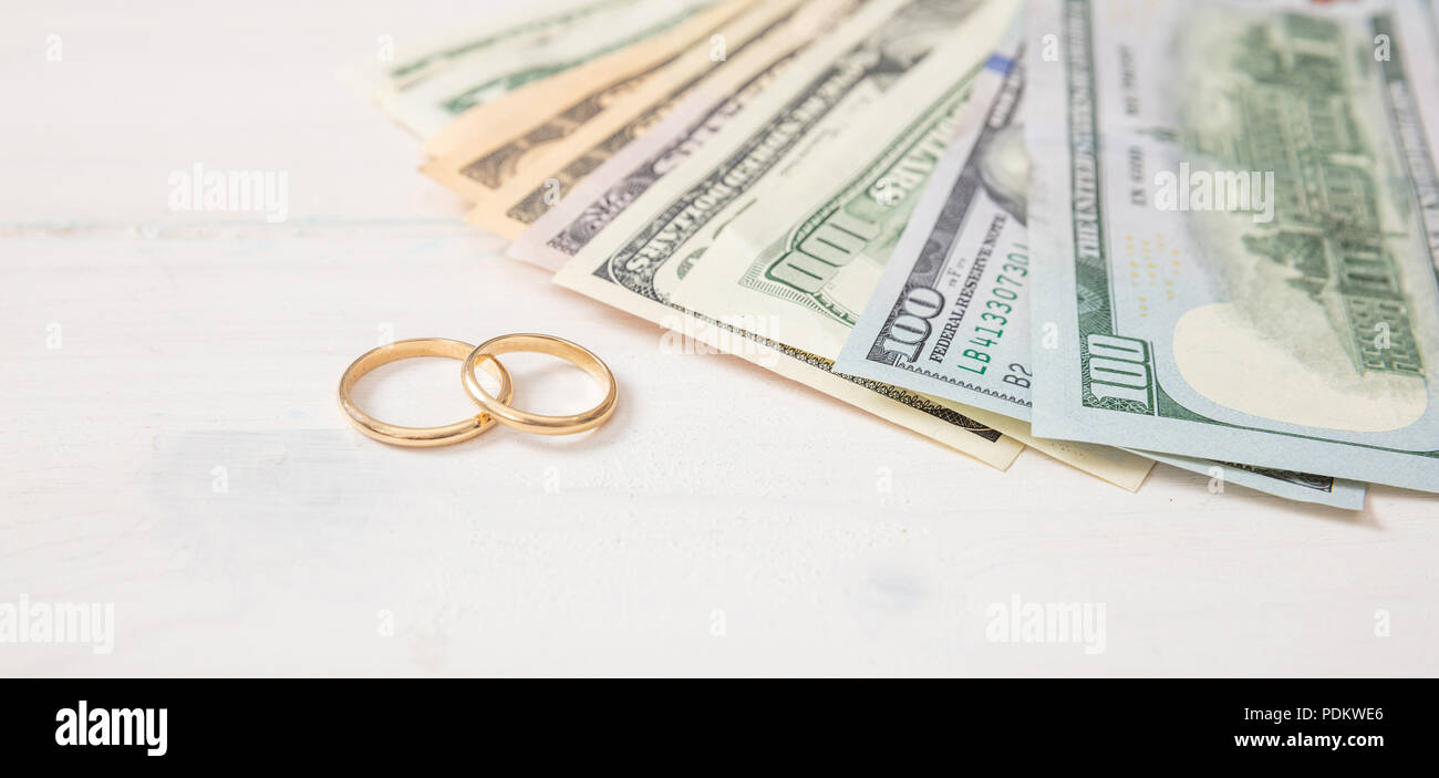 Ehe und Aufwendungen Konzept. Goldene Hochzeit Ringe und Banknoten Dollar, auf einem weißen Hintergrund Holz, Banner. Stockfoto