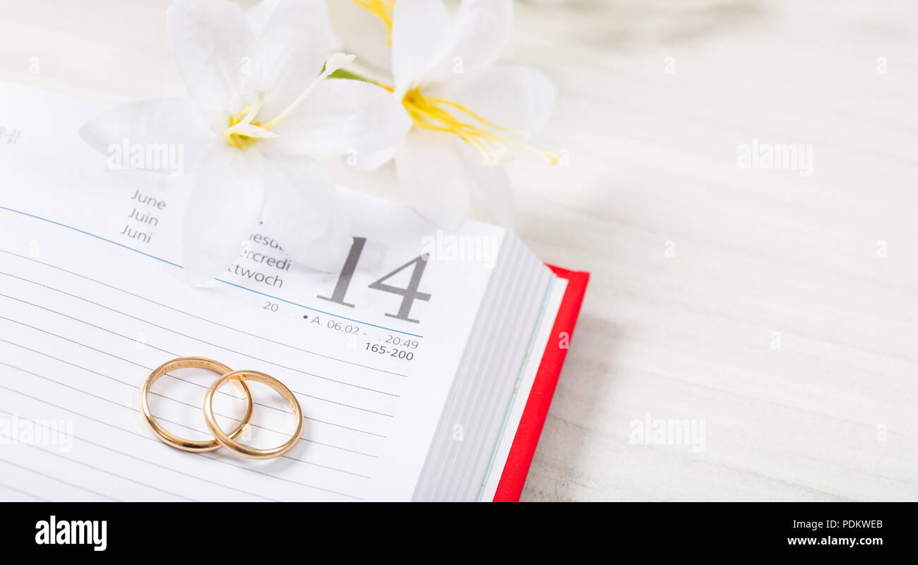 Planung ehe Konzept. Blick von oben auf die goldene Hochzeit Ringe und Blumen auf einem Kalender, auf einem weißen Holz- Tisch. Stockfoto