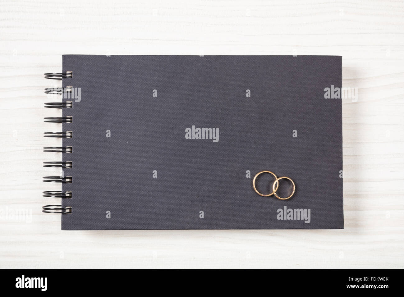 Liebe und Ehe Konzept. Goldene Hochzeit Ringe auf einem Schwarz notebook, Ansicht von oben, isoliert und kopieren Sie Raum, auf einem weißen Holz- Hintergrund. Stockfoto