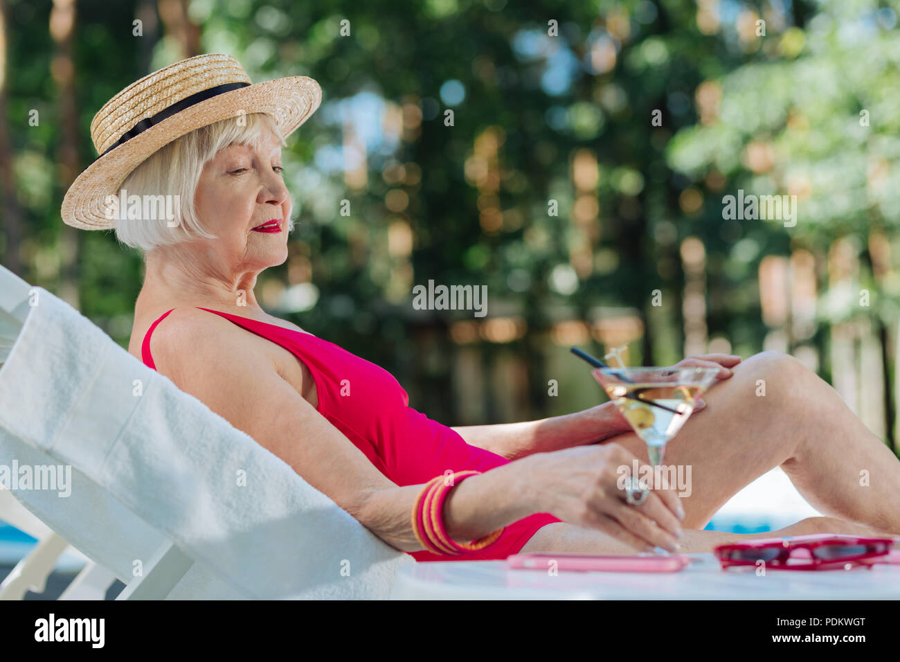 Blonde reife Frau mit Strohhut liegen in der Nähe des Pool Stockfoto