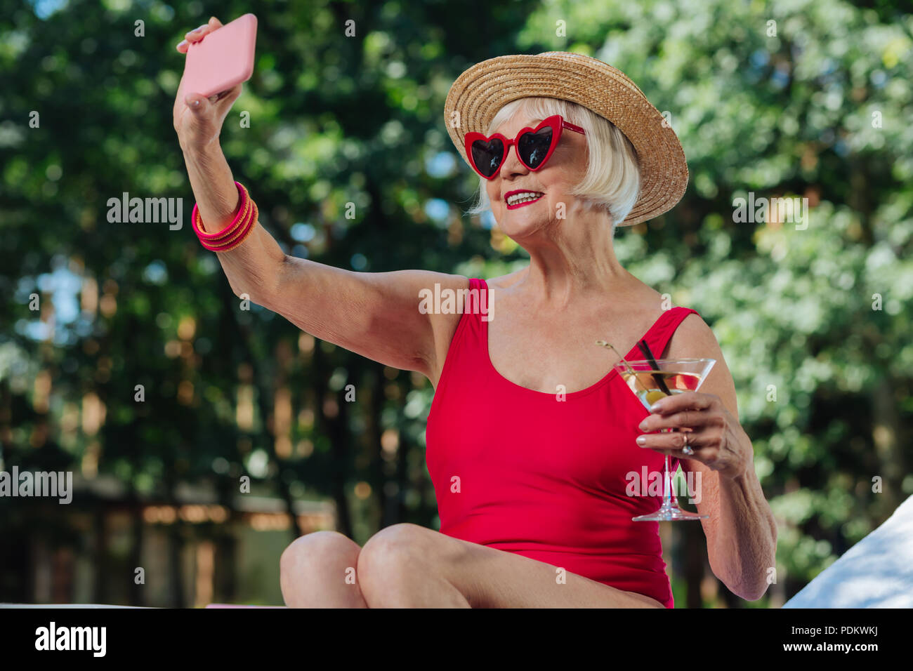 Strahlende blonde reife Frau, die Foto mit Martini Stockfoto