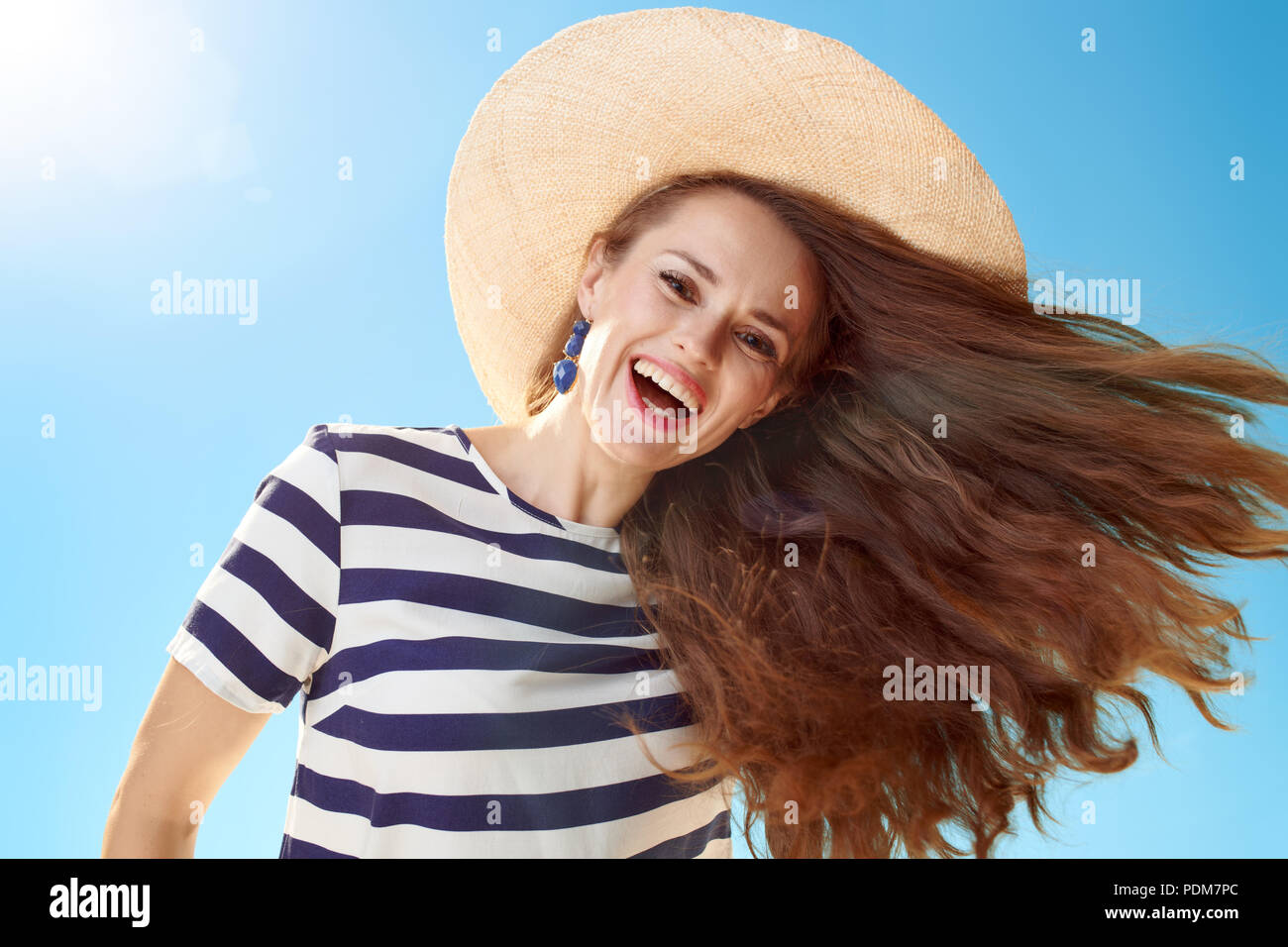 Lächelnd stilvolle Frau in Stroh Hut mit flatternden Haare gegen den blauen Himmel Stockfoto