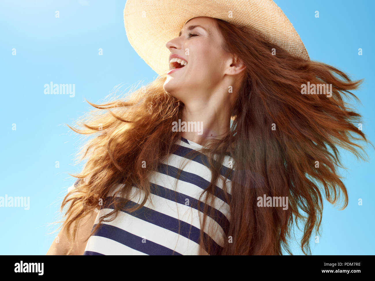 Gerne stilvolle Frau in Stroh Hut mit flatternden Haare gegen den blauen Himmel Stockfoto