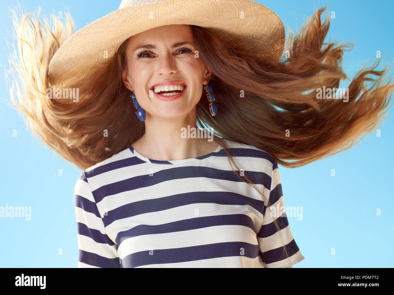 Glückliche junge Frau in Stroh Hut mit flatternden Haare gegen den blauen Himmel Stockfoto