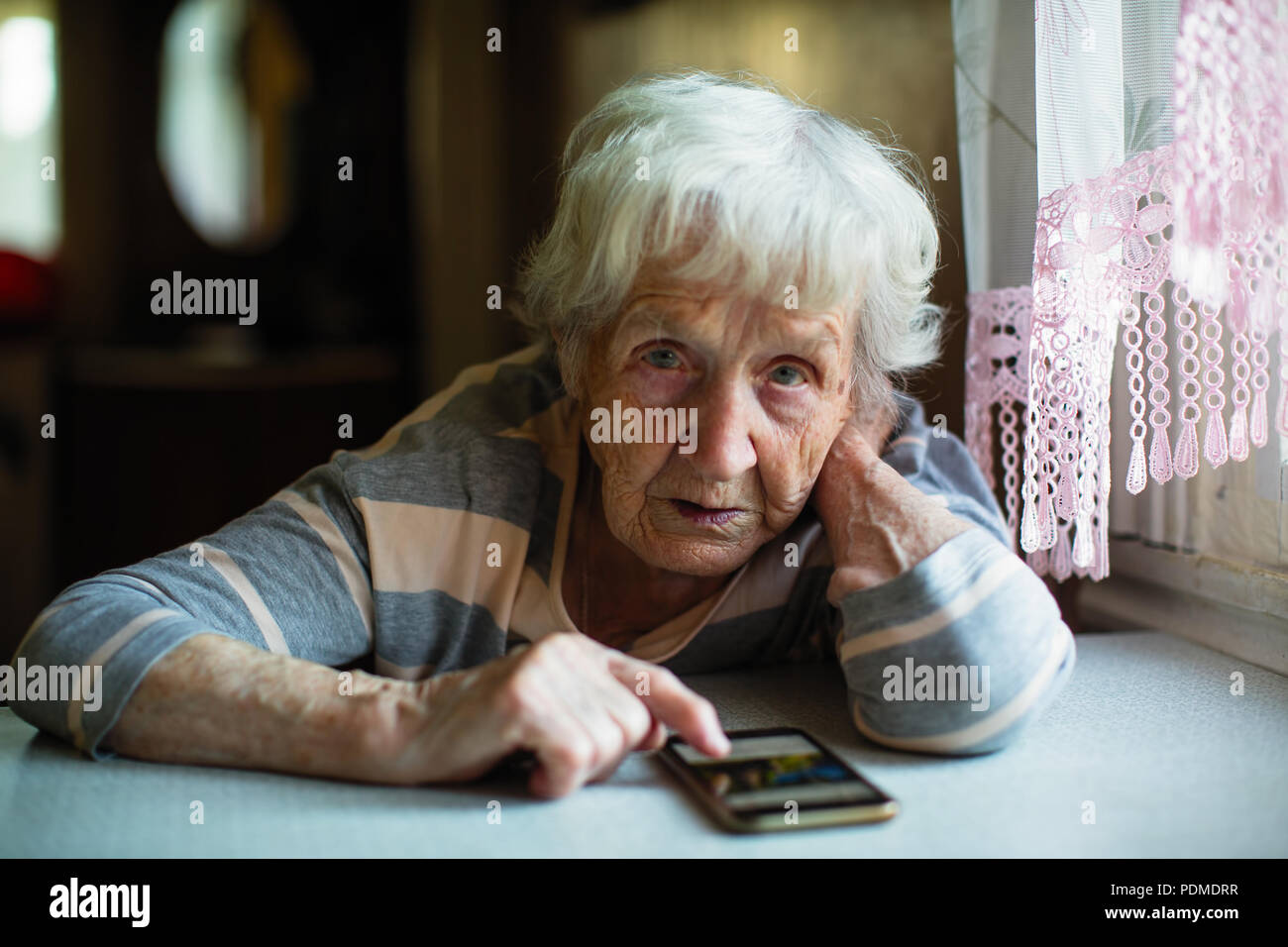 Eine ältere Frau mit einem Smartphone am Tisch sitzen. Stockfoto