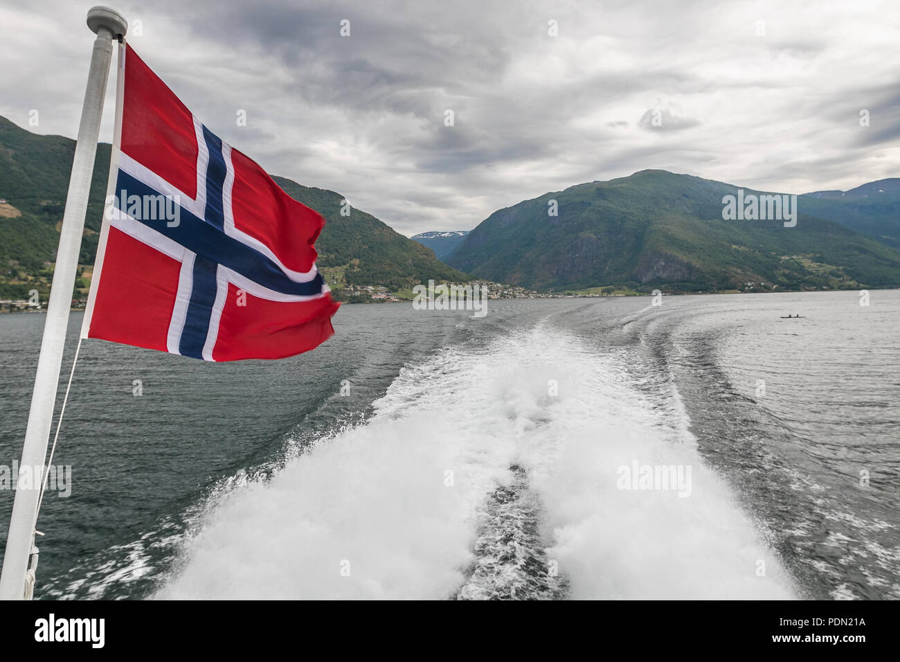 Norwegische Flagge ist das Fliegen am Heck eines Bootes durch einen Fjord reisen. Stockfoto