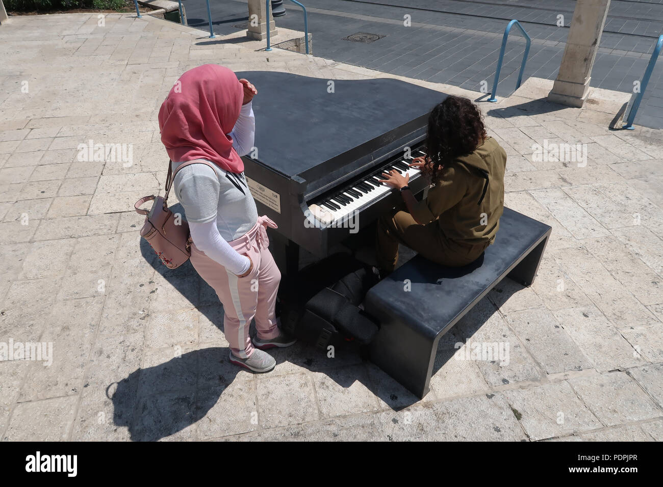 Eine junge palästinensische Mädchen sehen Sie eine israelische Soldatin spielen ein Klavier aus Beton durch die Kadenz in Safra Square auf der Jaffa Road West Jerusalem Israel Stockfoto