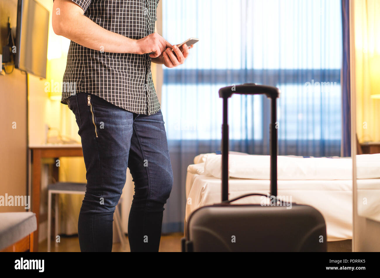 Mann mit Smartphone im Hotel Zimmer mit Gepäck und Koffer. Tourist mit Handy in Ferienwohnung. Aufruf Taxi. Stockfoto