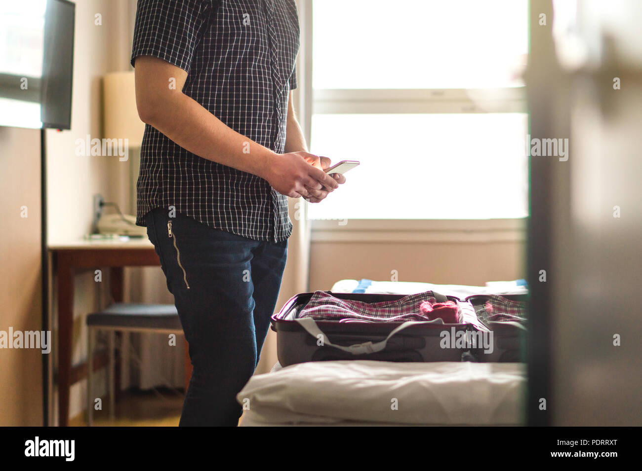 Mann mit Smartphone im Hotel Zimmer mit Gepäck und Koffer auf dem Bett. Handy und Verpackung. Gerade angekommen oder verlassen. Stockfoto