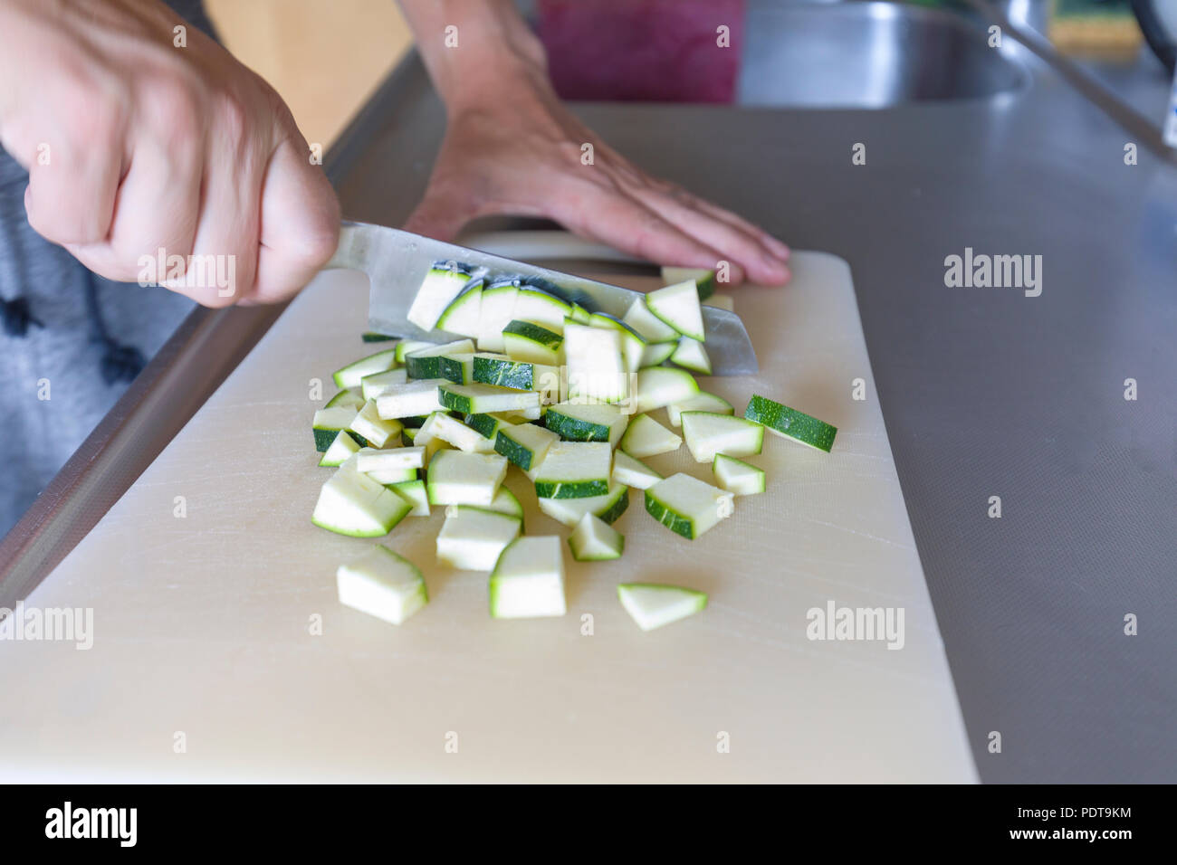 Einblick in die Hände von Person zu hacken, Zucchini aka Zucchini mit Küchenmesser in der Vorbereitung für Abendessen Stockfoto