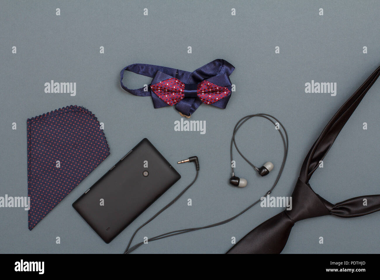 Taschentuch, Mobiltelefon, Kopfhörer, Fliege und Krawatte auf grauem Hintergrund. Zubehör für Männer. Ansicht von oben Stockfoto