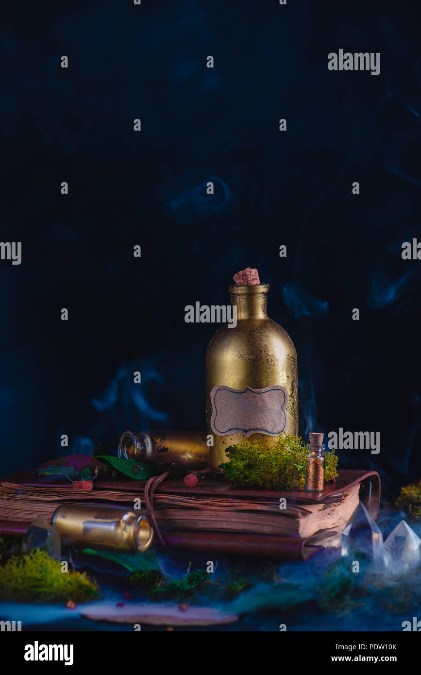 Goldene Zaubertrank Flasche in ein Stillleben mit einer okkulten Ausrüstung auf einem dunklen Hintergrund. Hexe oder Zauberer Arbeitsplatz mit kopieren. Stockfoto