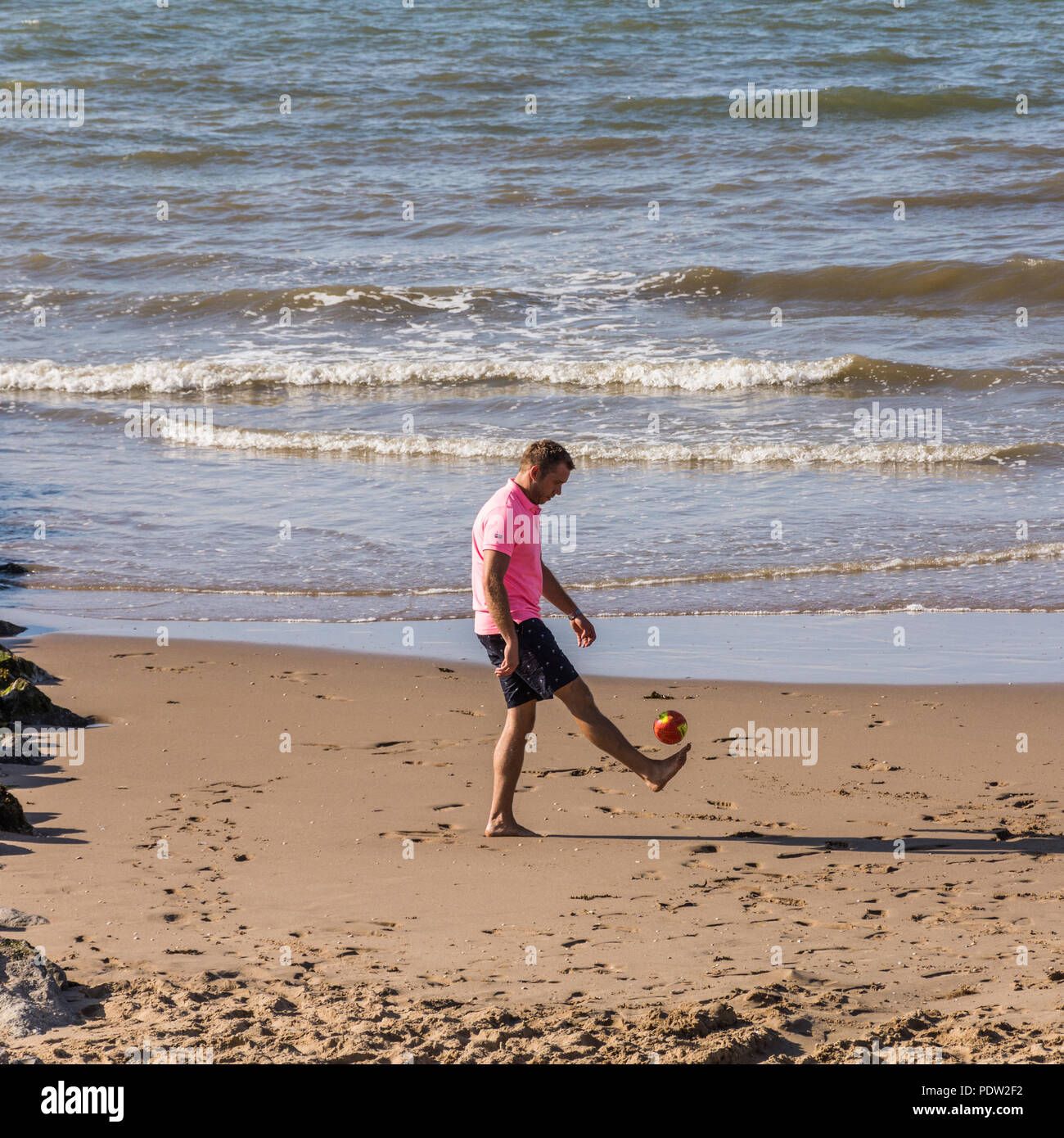 Mann treten eines kleinen Fußball am Strand, Prestatyn, North Wales, UK, während der Hitzewelle im Sommer 2018. Stockfoto