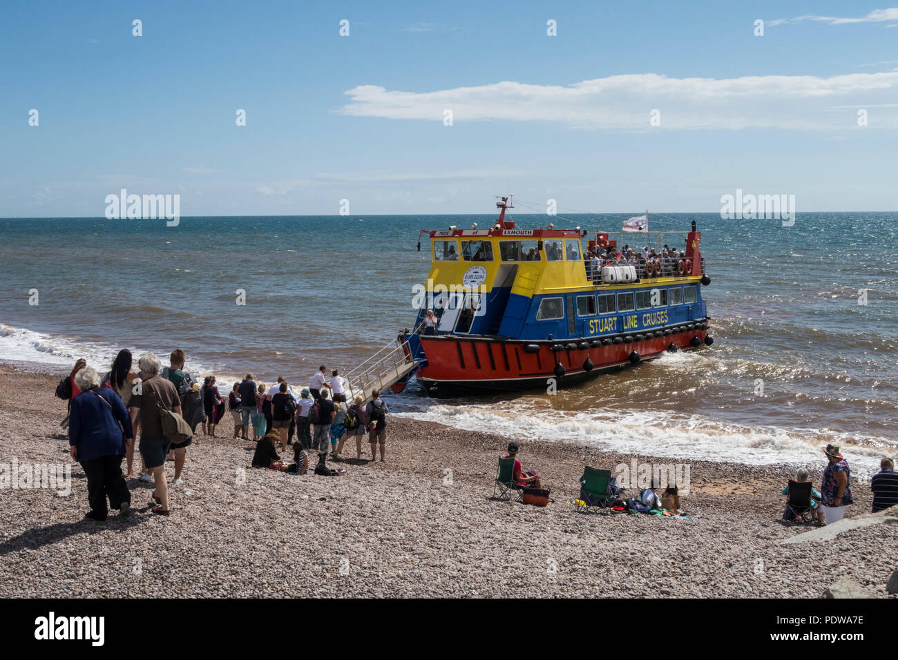 Touristen Warteschlange Board der Stolz von Exmouth, ein Stuart Line coast Cruiser zu, wie es landet in Sidmouth Strand. Stockfoto